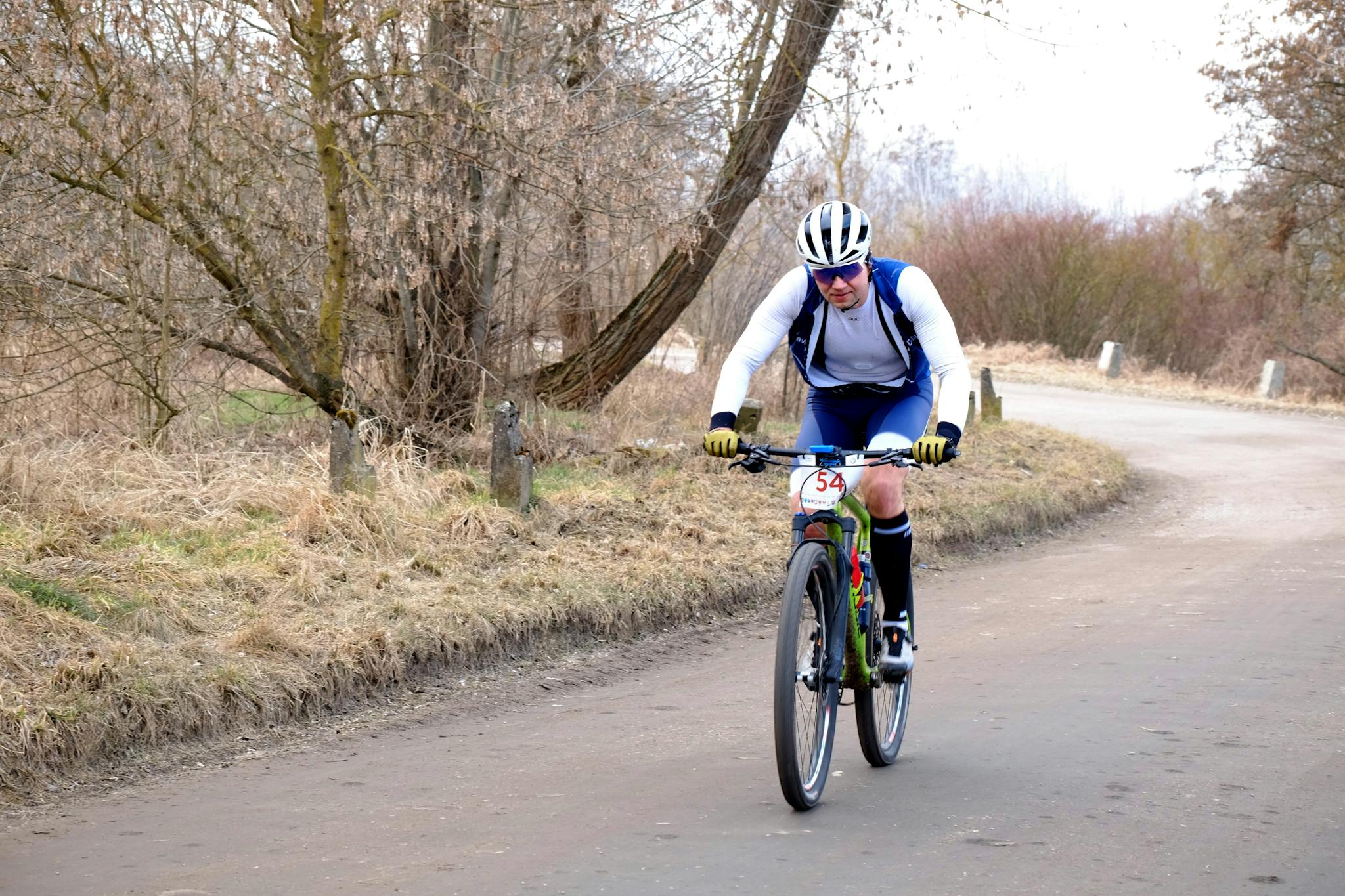 Cyclist in helmet and gear competing in an outdoor race on a rural road lined with trees.