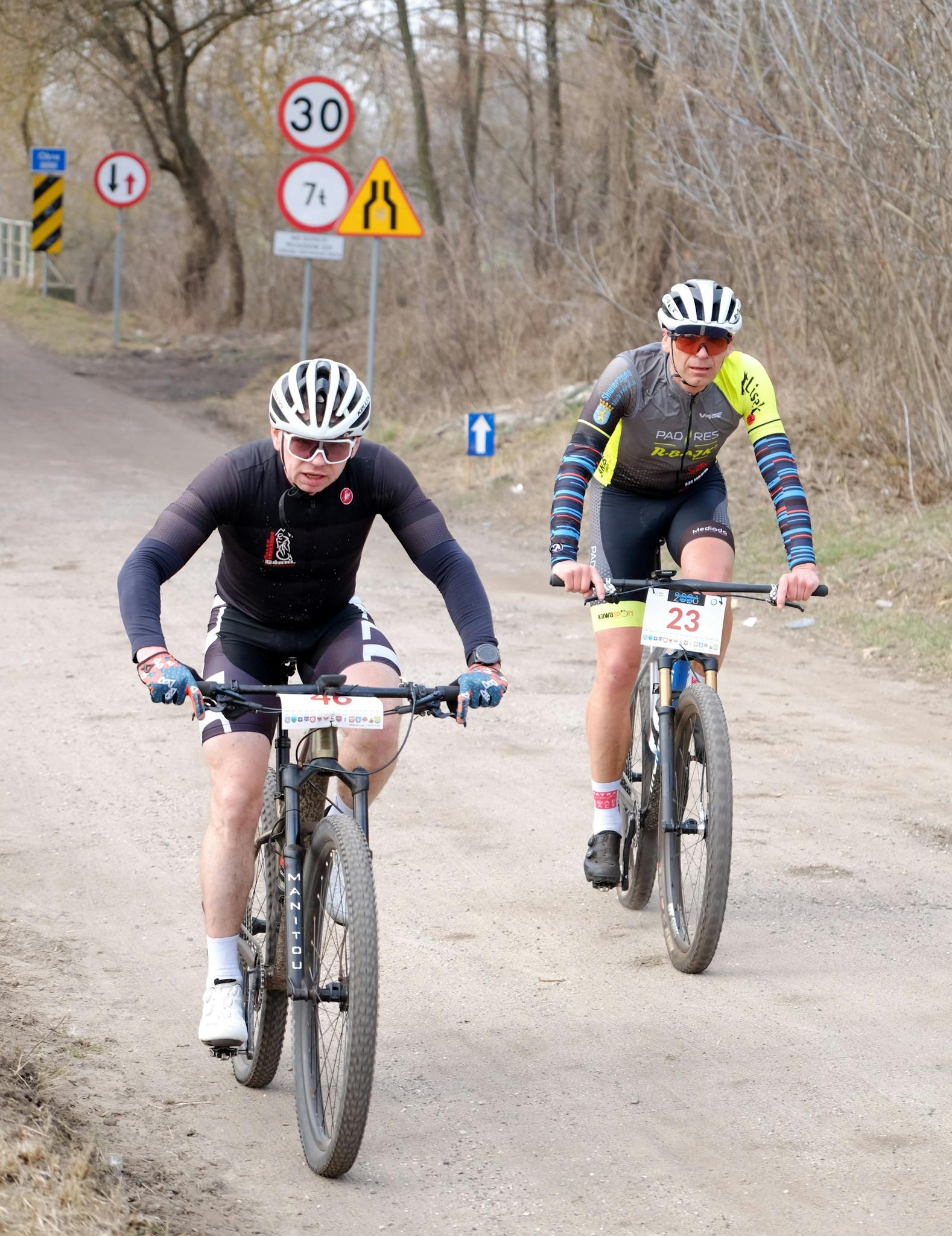 Two male cyclists riding on a dirt road during a competitive outdoor race.